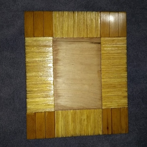 May include: A wooden picture frame crafted from thin strips of wood, arranged in a grid pattern. The frame is stained a light brown colour and has a natural wood finish.