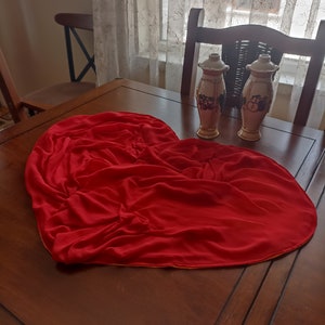 May include: A red heart-shaped tablecloth on a wooden table with two decorative ceramic vases with floral designs.
