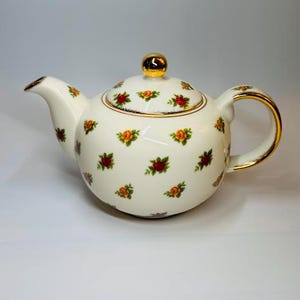 May include: A white porcelain teapot with a gold handle, spout, and rim. The teapot is decorated with small floral patterns in red, yellow, and green. The lid has a gold knob. A classic tea set item.