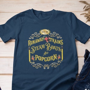 May include: A navy blue t-shirt with a vintage-style graphic design featuring the text "Give me runaway trains, steam boats and popcorn".