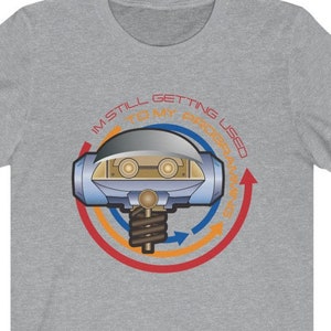 May include: A heather grey t-shirt with a blue and yellow robot graphic and the text "I'm still getting used to my programming".