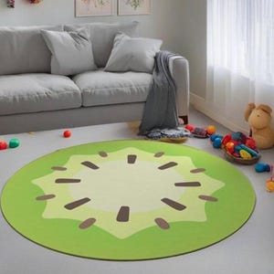 May include: A round green and yellow rug with a kiwi fruit design. The rug has a brown center and a green outer edge. The rug is on a light gray floor.