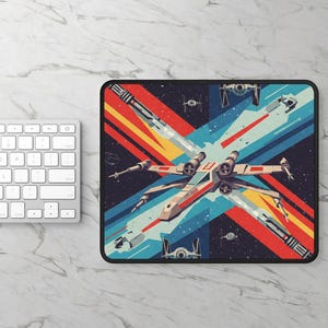 May include: A rectangular mousepad featuring a stylized illustration of an X-wing fighter in a space battle. The design incorporates red, orange, yellow, and blue stripes, with a black border. Additional space fighter details are included.