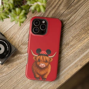 May include: Red phone case with a cartoon Highland cow wearing a red and white polka dot Mickey Mouse hat.