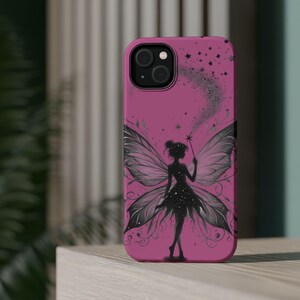May include: A magenta smartphone case featuring a black silhouette of a fairy with large, detailed wings. The fairy holds a star-tipped wand, with a trail of sparkling stars and swirling lines extending upward against the solid magenta background.