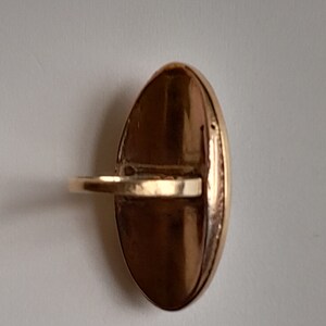May include: A gold oval ring with a smooth, shiny surface. The ring has a simple band and a large oval-shaped top.