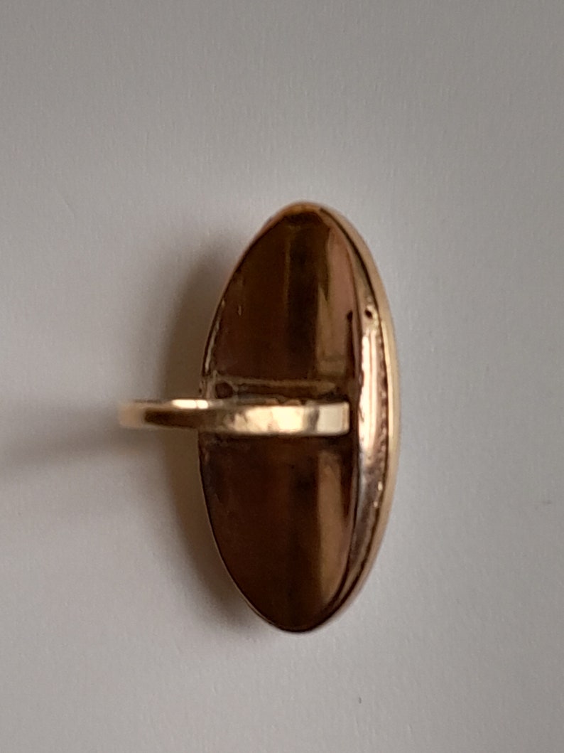 May include: A gold oval ring with a smooth, shiny surface. The ring has a simple band and a large oval-shaped top.