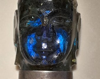 May include: A silver pendant featuring a carved face of a Buddha made from iridescent labradorite gemstone.