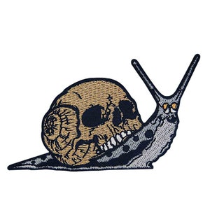 Peut inclure: Écusson brodé représentant un escargot avec une coquille en forme de crâne. Le crâne est beige avec des orbites et des dents noires. Le corps de l'escargot est gris avec des taches et des antennes noires. Un écusson unique sur le thème gothique.