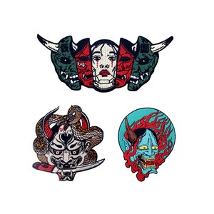 May include: Three embroidered patches featuring Japanese demon masks. The first patch is a green, red, and white mask with a female face. The second patch is a black and white mask with a snake design. The third patch is a blue and red mask with flames.