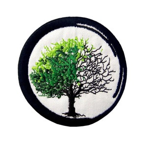 Pode incluir: Um remendo bordado em preto e branco com uma árvore verde e marrom no centro. A árvore é metade verde e metade marrom, simbolizando a vida e a morte.