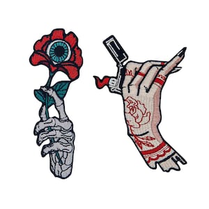 May include: Two embroidered iron-on patches. One features a skeleton hand holding a red rose with an eye in the center. The other features a hand with a tattoo of a rose and a lighter.