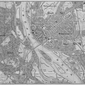 Op de afbeelding: Een zwart-witte kaart van Riga, Letland, met de titel "PLAN VON RIGA" in de rechterbovenhoek. De kaart toont de indeling van de stad, inclusief de rivier de Daugava, straten en wijken. De kaart is verdeeld in secties met de labels "Petersburger Stadt - Teil", "Moskauer Stadt - Teil" en "Stadt - Teil".