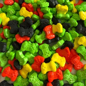 May include: A close-up shot of a pile of colorful, candy-shaped video game controllers. The controllers are in various colors, including green, red, yellow, and black. The candy is a fun and playful treat.