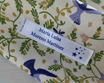 May include: White fabric with a floral pattern featuring blue birds. A white label with blue text reads "Maria Luisa Moreno Martinez" and has blue stars in the corner.
