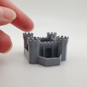 May include: A miniature grey castle model, 3D-printed with four turrets and an arched entrance. The small castle is a detailed replica, showcasing architectural features. The model is a solid grey colour.