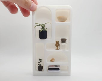 May include: White shelf unit with five shelves, featuring two potted plants, a small glass jar, a gold goblet, and a small wooden bowl.