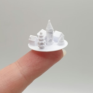 May include: A white 3D printed miniature village scene with a church, houses, and a tree on a small round base.