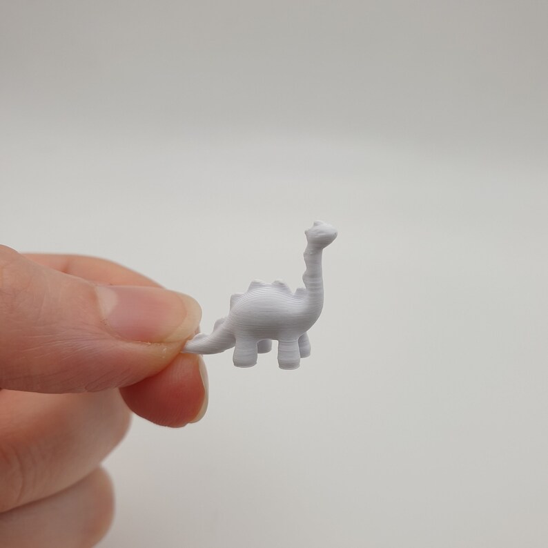 May include: A small white plastic dinosaur figurine. The dinosaur is standing on all fours and has a long neck.