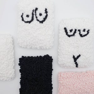 May include: Four small, square, fluffy, hand-stitched pillows with embroidered designs. Two pillows are white with black embroidered breasts, one pillow is black, and one pillow is pink.