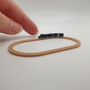 May include: A miniature train set with a brown track in the shape of an oval. The train is made up of several black carriages.