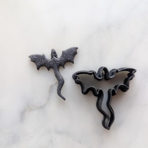 Peut inclure: Deux emportes-pièces en forme de dragon noir, l'un uni et l'autre avec un design détaillé. Les emportes-pièces sont sur une surface en marbre blanc.