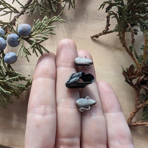 May include: Three small, gray, ceramic mice figurines with red eyes. The mice are sitting on a hand.