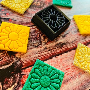 May include: A set of six colourful silicone moulds for making decorative flower-shaped cookies or fondant. The moulds are in the shape of a flower with a raised centre and petals. The moulds are yellow, green, and black.