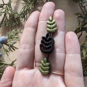 May include: Three small, decorative, leaf-shaped ornaments. Two are gold and one is black.