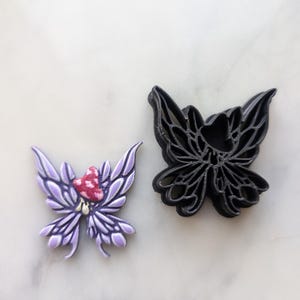 May include: A purple butterfly cookie cutter with a red mushroom on its head and a black butterfly cookie cutter.