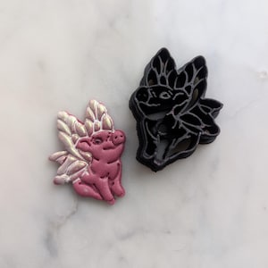 May include: A pink pig with gold wings cookie cutter and a black pig with wings cookie cutter.