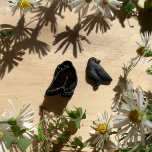 May include: Two black crow cookie cutters on a wooden surface surrounded by white daisies.