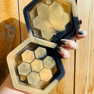 May include: A black and gold resin tray with a hexagonal design. The tray is divided into multiple compartments, each with a hexagonal shape.