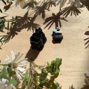 May include: Two black silicone cookie cutters, one shaped like a cauldron and the other shaped like a bunny rabbit. The bunny rabbit cutter has a white glaze on the inside.