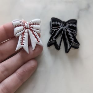 Puede incluir: Un cortador de galletas de lazo de béisbol blanco y rojo con un cortador de galletas de plástico negro en el fondo.