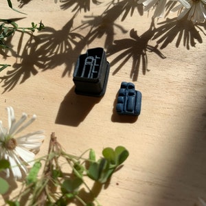 May include: Two black silicone moulds for baking. The larger mould is shaped like a house with a chimney and windows. The smaller mould is shaped like a small rectangular box.