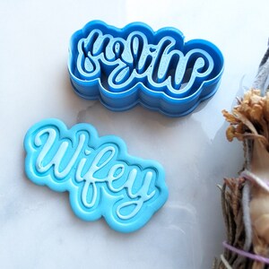 Puede incluir: Dos cortadores de galletas de plástico azul, uno con forma de la palabra "wifey" y el otro con forma de la palabra "hubby".