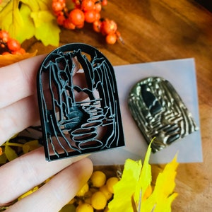 Peut inclure: Un tampon en polymère noir avec un motif détaillé d'un chemin menant à travers une forêt. Le tampon est tenu dans une main sur un fond de feuillage d'automne.