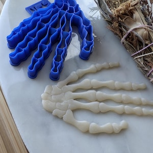 May include: A blue plastic skeleton hand cookie cutter and a white fondant skeleton hand.