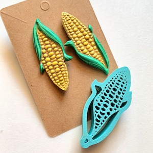 May include: Two yellow and green corn on the cob earrings and a blue corn on the cob mould.