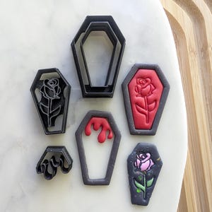 Puede incluir: Conjunto de seis cortadores de galletas de metal negro con forma de ataúd. Algunos ataúdes tienen un diseño de rosa, uno tiene un diseño de sangre goteando y otro tiene un diseño ondulado.
