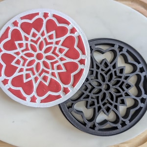 Könnte beinhalten: Zwei runde Untersetzer mit einem Mandala-Design. Ein Untersetzer ist weiß mit einem roten Mandala-Design und der andere ist schwarz mit einem schwarzen Mandala-Design.