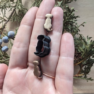 May include: Three small dog-shaped cookie cutters. Two are gold and one is black.