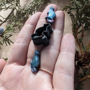 May include: Three small, blue, ceramic mice figurines. The mice are in different poses, one is sitting up, one is standing, and one is curled up. The figurines are on a person's hand.