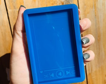 May include: A vibrant blue silicone mold in a rectangular shape, featuring a music player interface design. The mold includes play, pause, skip, and like icons. The mold is held in a hand.