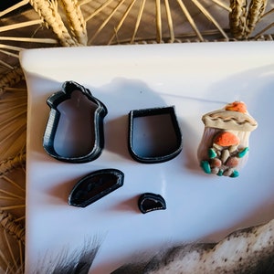 Puede incluir: Un juego de cinco cortadores de galletas de plástico negro en forma de botella, vaso, sombrero, taco y medio círculo. Los cortadores están sobre una superficie blanca.