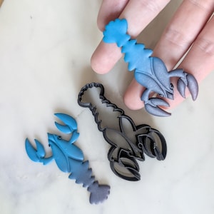 May include: Three lobster-shaped cookie cutters, two are black and one is blue. The blue cutter is made of fondant and the black cutters are made of plastic.