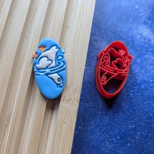 Puede incluir: Dos cortadores de galletas, uno azul y otro rojo, con forma de pájaro en vuelo. El cortador azul tiene un diseño de pájaro blanco, mientras que el cortador rojo tiene un diseño de pájaro rojo.