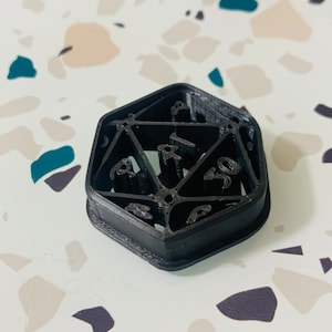 May include: A black plastic 3D printed D20 dice with the numbers 1 through 20 printed on the faces.