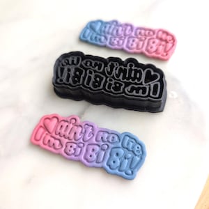 May include: Three silicone cookie cutters with different phrases. The first cutter is black and says "All an 'I'm fin' is big is on!" The second cutter is pink and blue and says "Ain't no lie I'm Bi Bi Bi!" The third cutter is also pink and blue and says "Ain't no lie I'm Bi Bi Bi!"